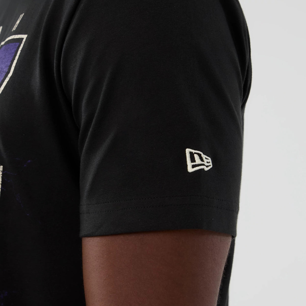New Era Utah Jazz NBA Hardwood Classic Black T-Shirt, side view showing a small white embroidered New Era logo on the short sleeve, with a view of the front design featuring purple and white graphics.