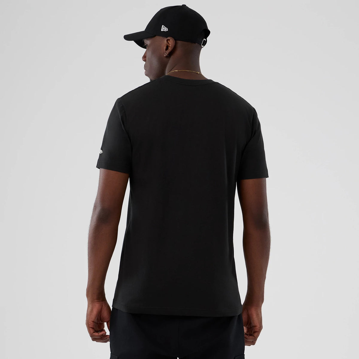 New Era Utah Jazz NBA Hardwood Classic Black T-Shirt, back view on a model with a matching black cap, featuring a plain black design with a small embroidered New Era logo in white on the left sleeve.