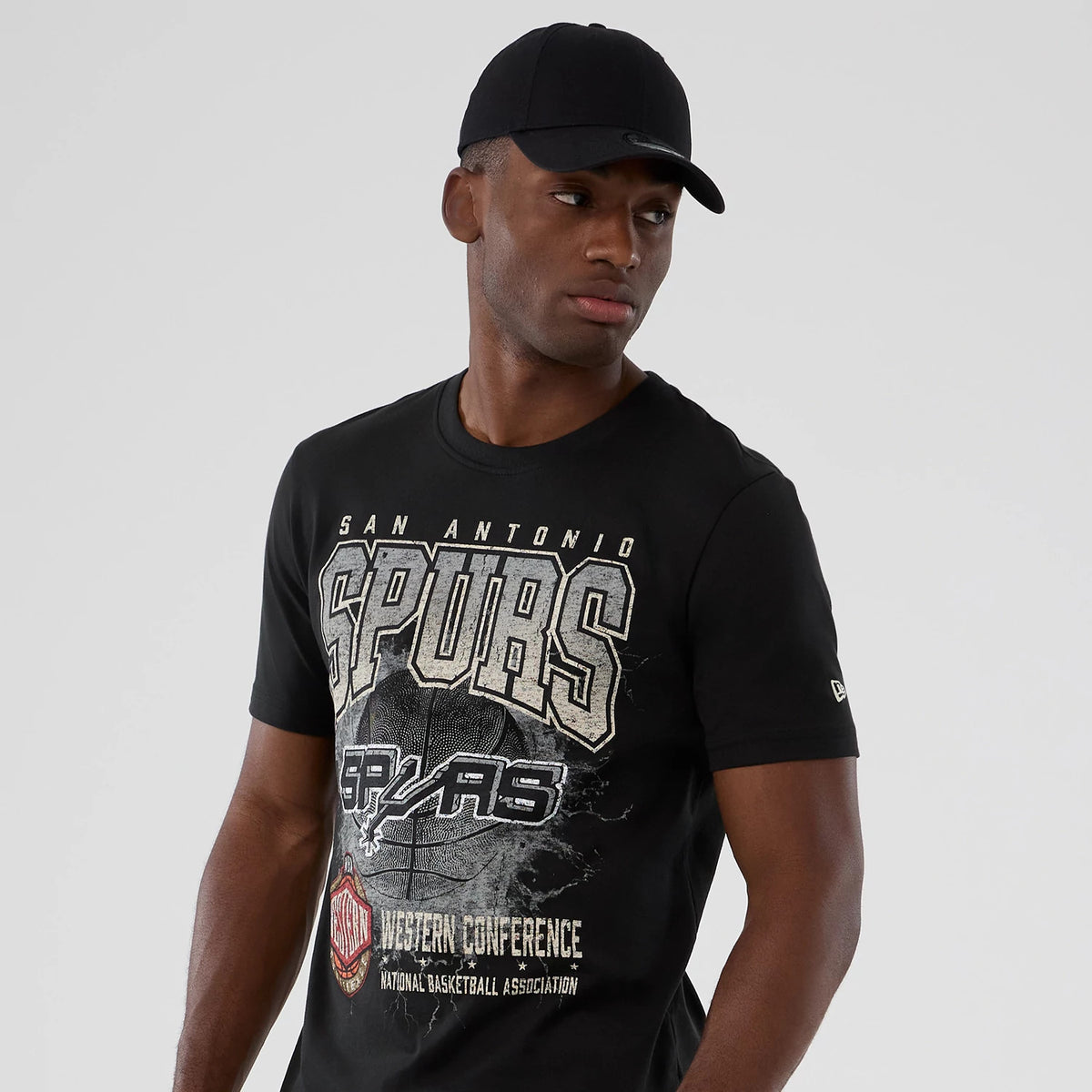 New Era San Antonio Spurs NBA Hardwood Classic Black T-Shirt, front view on a model wearing a black cap, showing Spurs lettering across the chest with an NBA logo beneath, and a small embroidered New Era logo on the sleeve.