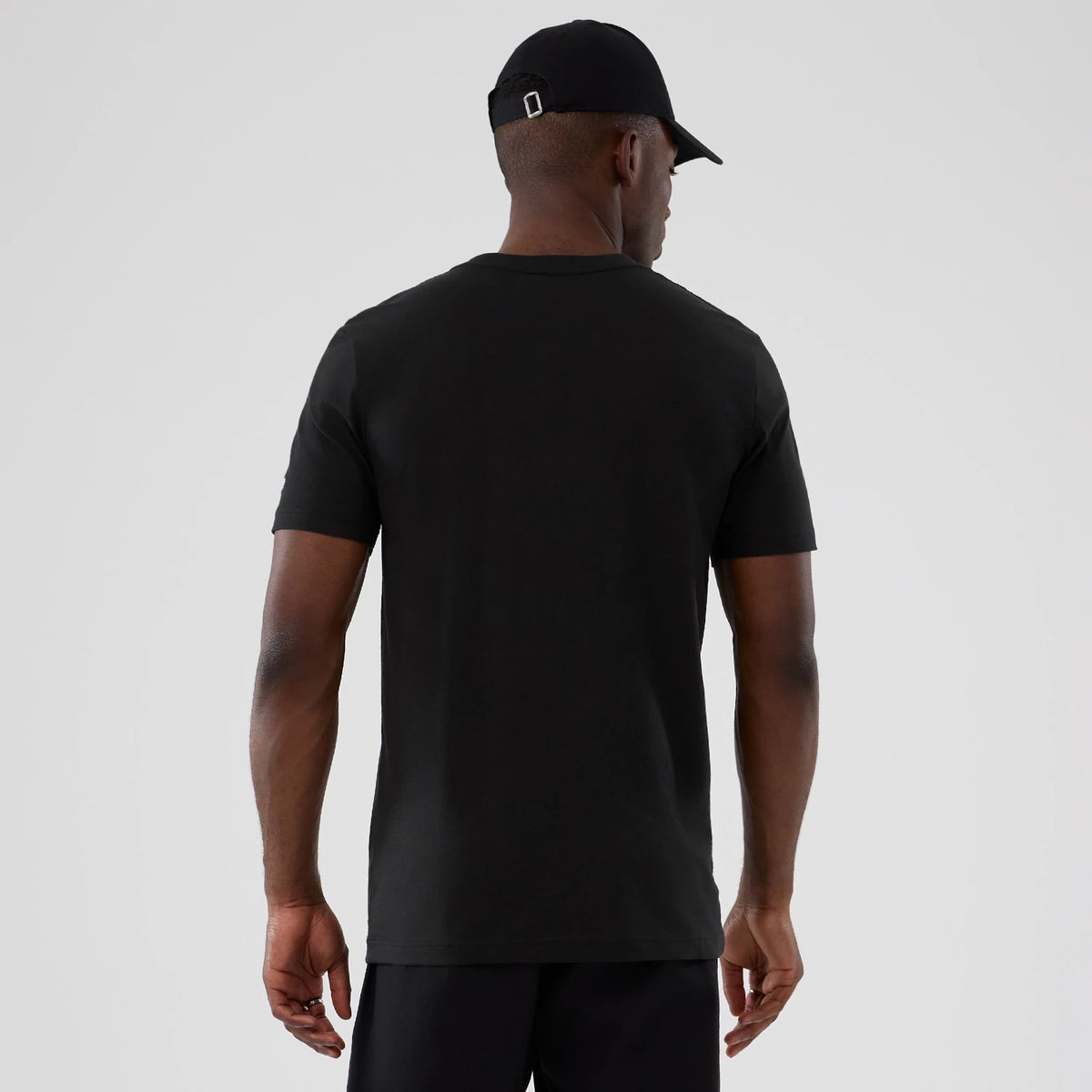 New Era San Antonio Spurs NBA Hardwood Classic Black T-Shirt, back view on-model showing the plain black design with short sleeves, paired with a black cap, focusing on the fit and length of the T-shirt over dark shorts.
