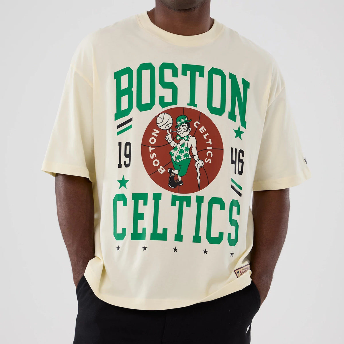 New Era Boston Celtics NBA Hardwood Classic Cream T-Shirt, front view on a model showing the green Boston Celtics lettering, 1946 in black, and the central team mascot graphic on the chest, with a small embroidered logo on the left sleeve.