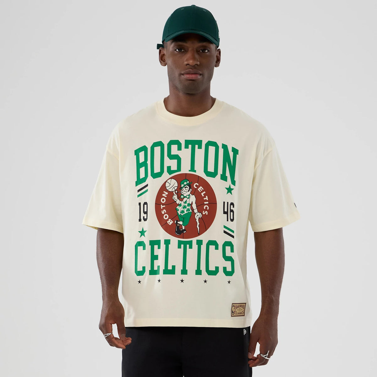 New Era Boston Celtics NBA Hardwood Classic Cream T-Shirt, front view on-model displaying a large green and brown Boston Celtics graphic with 1946 lettering and a small embroidered New Era logo on the left sleeve edge.