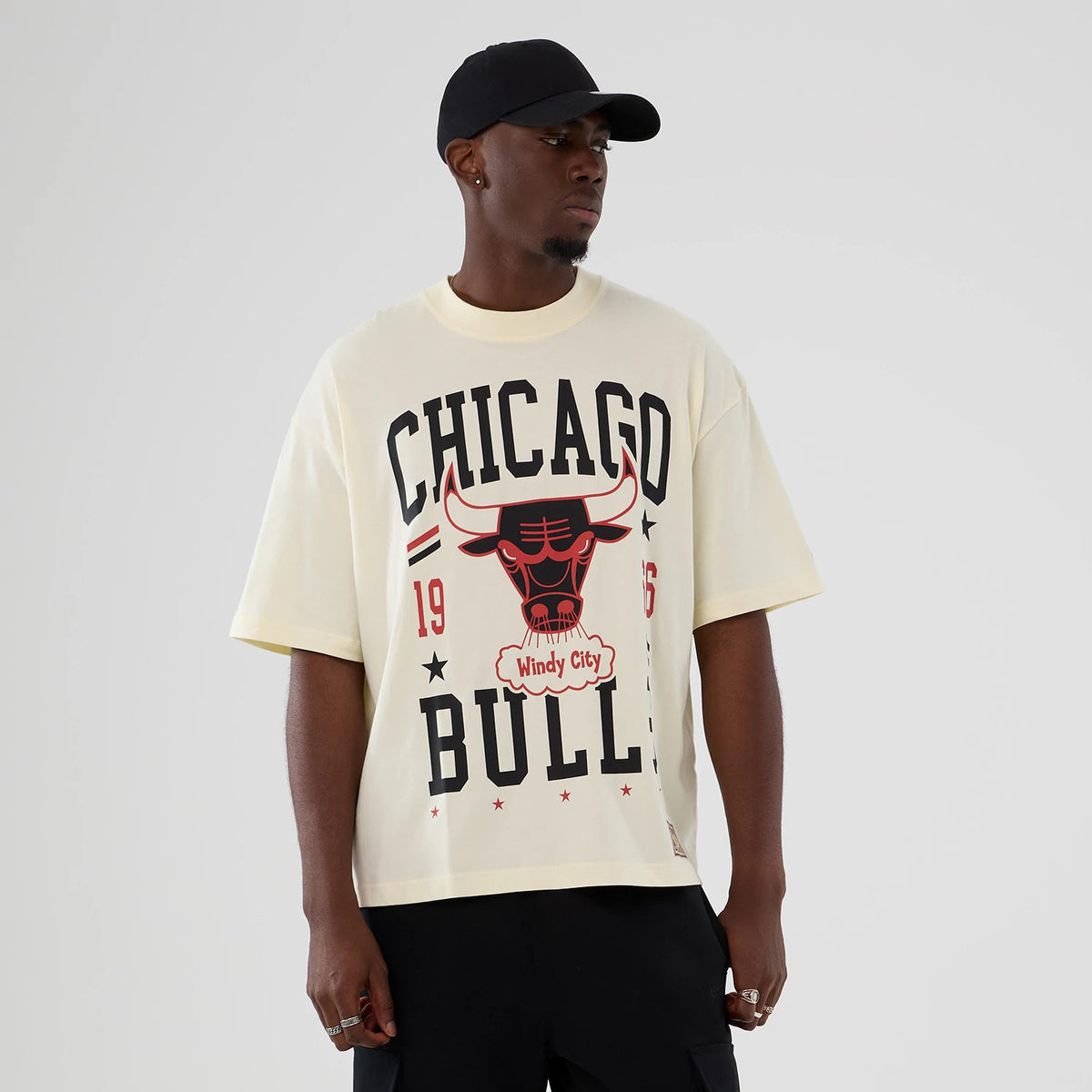 New Era Chicago Bulls NBA Hardwood Classic Cream T-Shirt, front view on a model displaying a black and red Bulls graphic and 1966 Chicago lettering, paired with a black cap for a casual look.