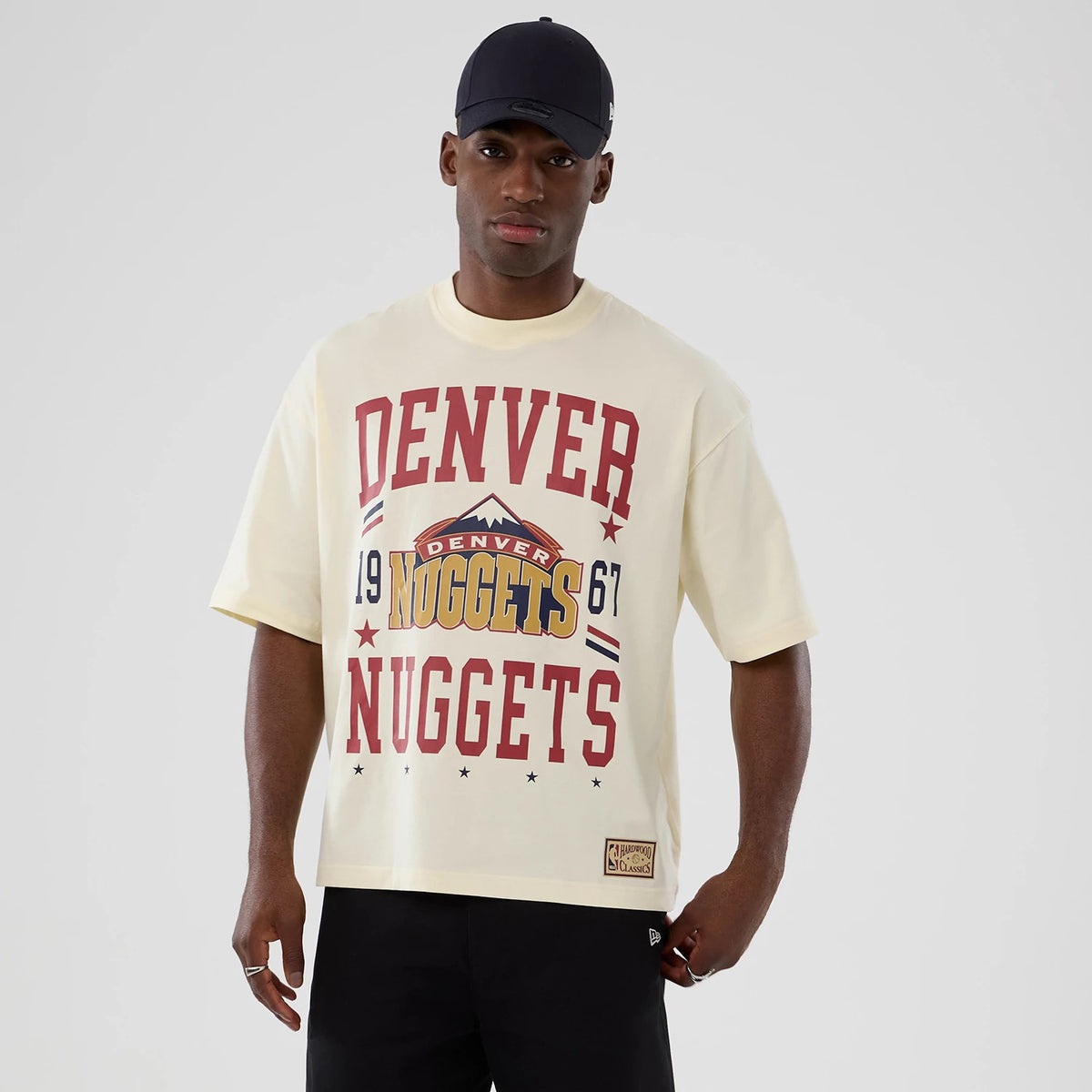New Era Denver Nuggets NBA Hardwood Classic Cream T-Shirt, front view on-model showing red Denver Nuggets lettering on a cream background, team logo at the chest centre, and a patch near the hem.