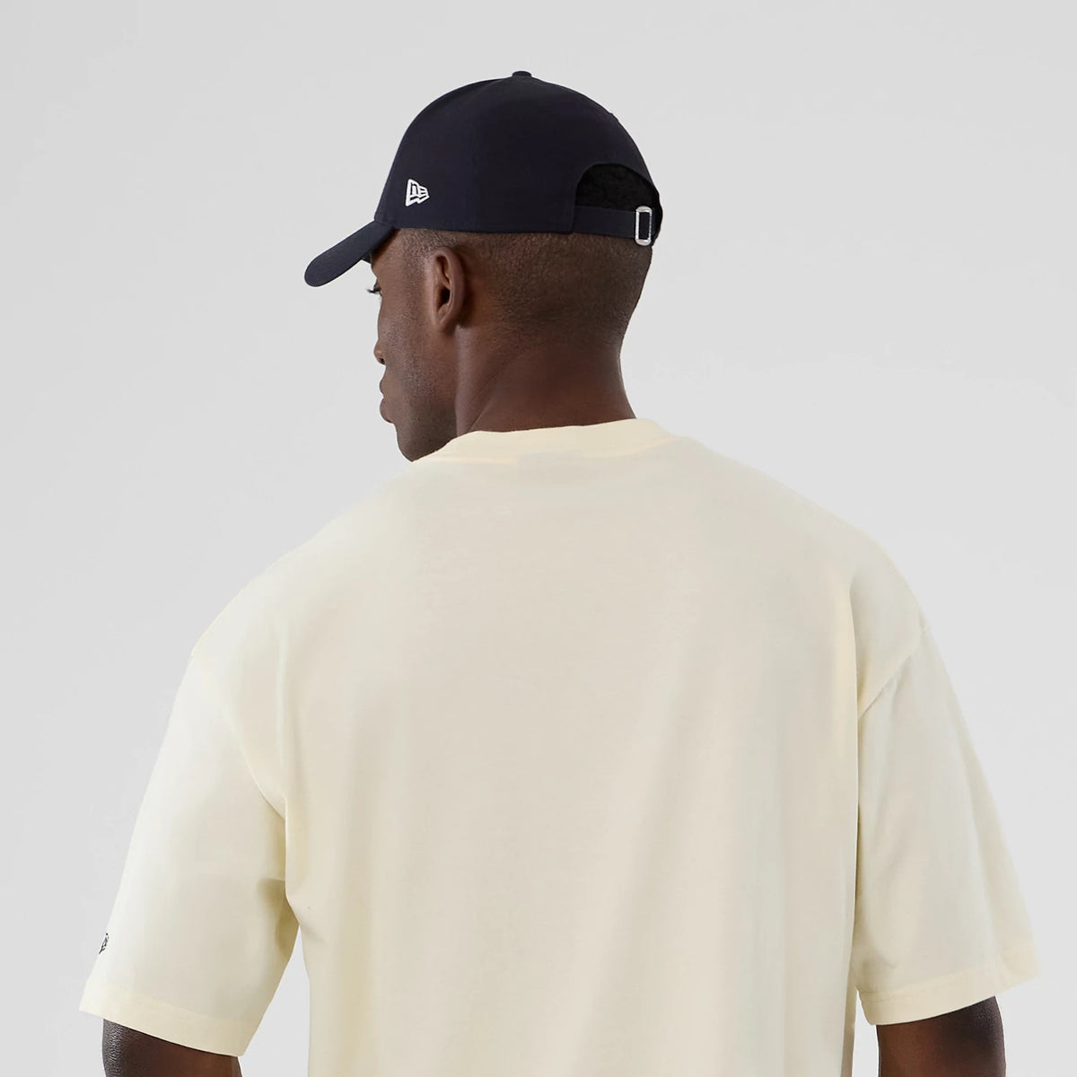 New Era Denver Nuggets NBA Hardwood Classic Cream T-Shirt, back view on-model showing the plain cream back with short sleeves, paired with a navy cap featuring an embroidered New Era logo on the side.