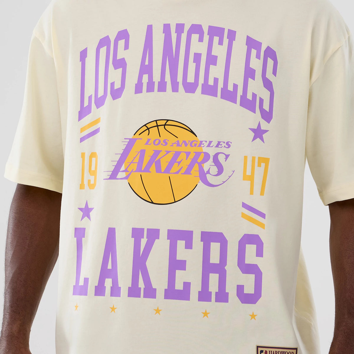 New Era LA Lakers NBA Hardwood Classic Cream T-Shirt, front view showing large purple Los Angeles Lakers lettering, a yellow basketball graphic and a printed Lakers logo centred on the cream fabric.