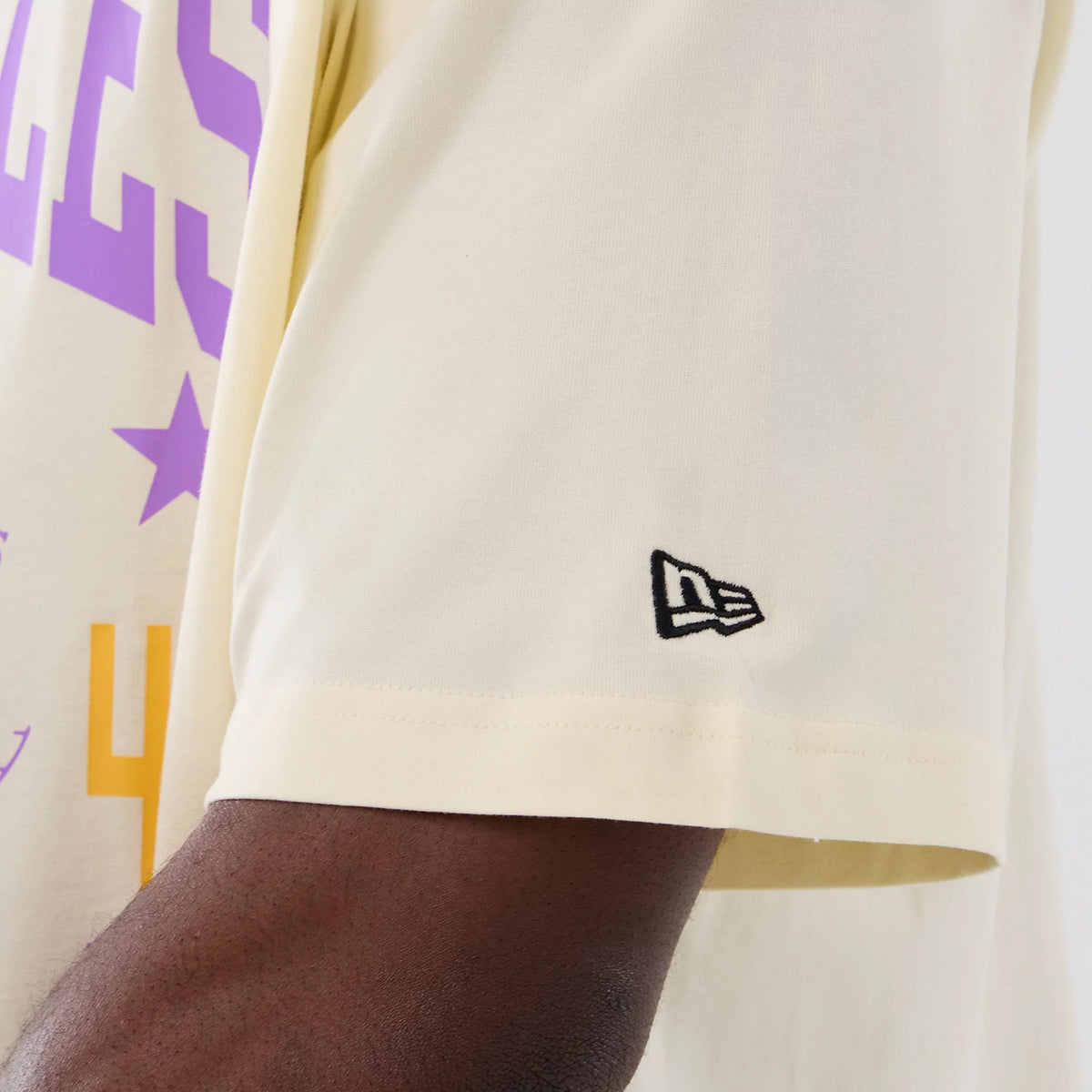 New Era LA Lakers NBA Hardwood Classic Cream T-Shirt, side view displaying purple graphic elements on the arm and a black embroidered New Era logo near the hem of the short sleeve.