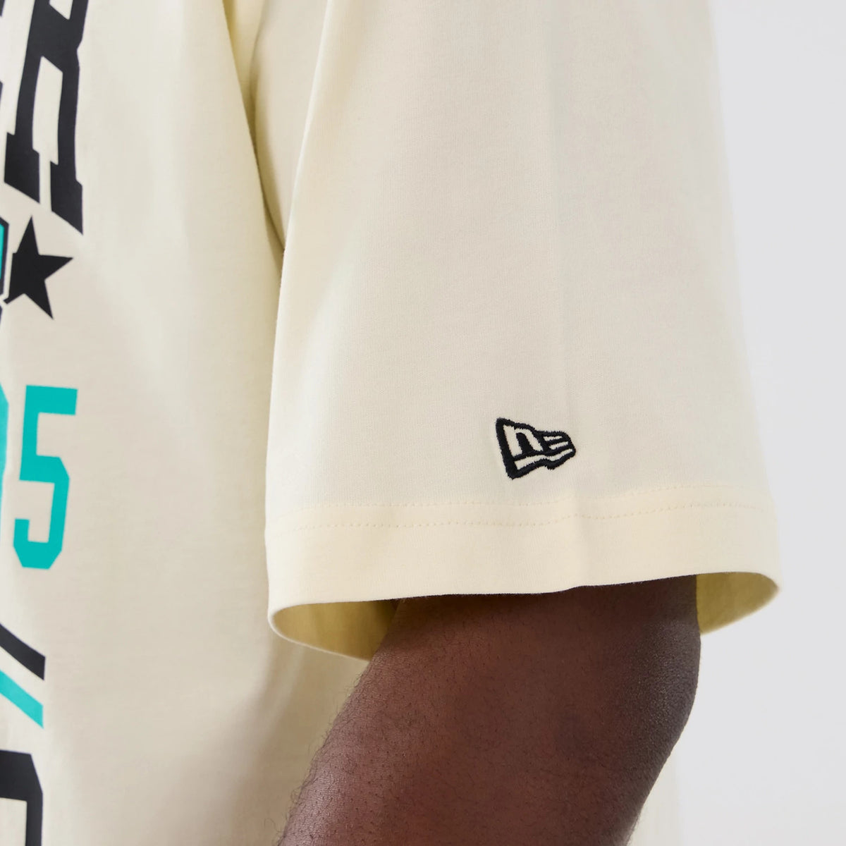 New Era Vancouver Grizzlies NBA Hardwood Classic Cream T-Shirt, close-up view of the sleeve featuring a black embroidered New Era logo near the cuff and part of the black and teal graphic design on the front.