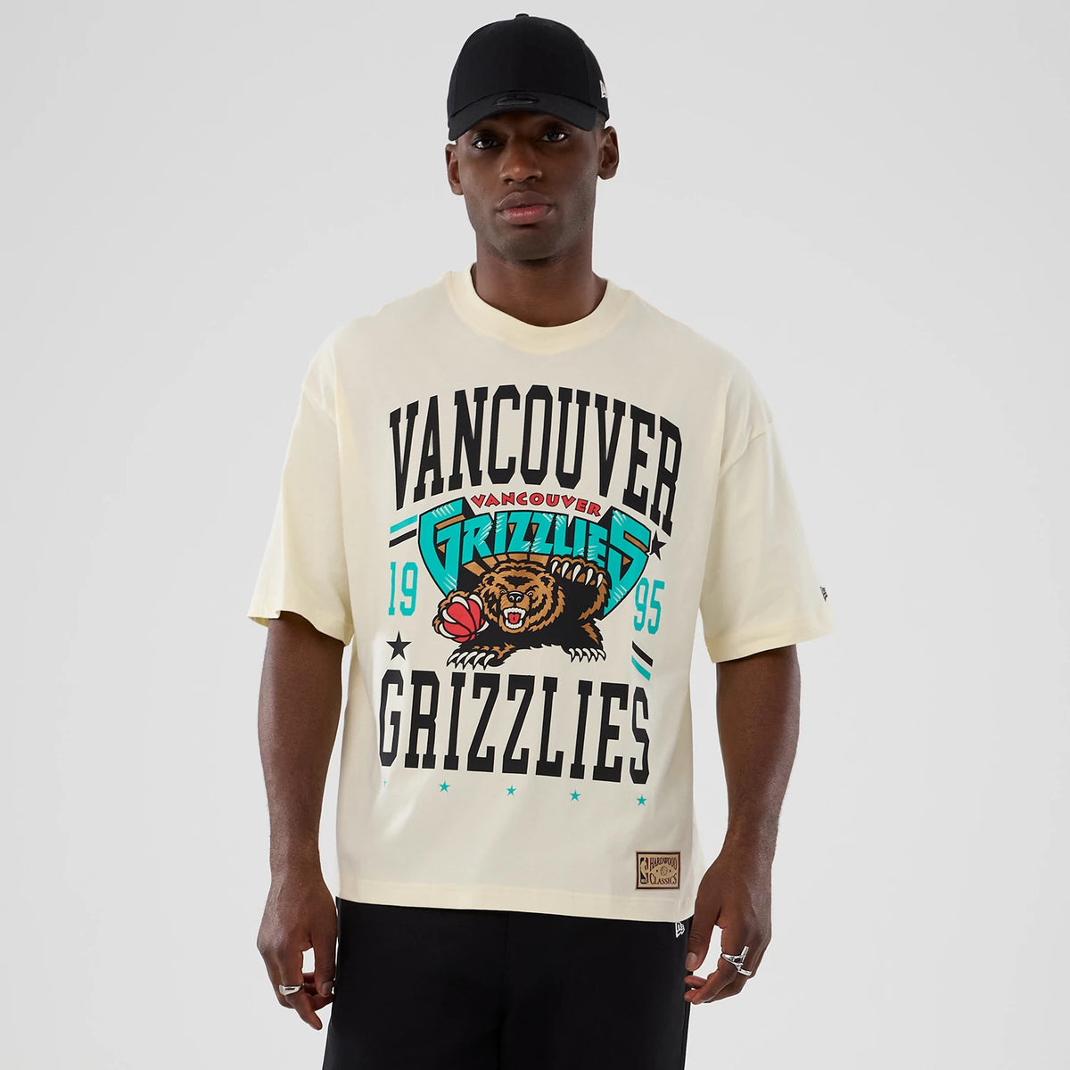 New Era Vancouver Grizzlies NBA Hardwood Classic Cream T-Shirt, front view on a model, featuring black Vancouver Grizzlies lettering, a graphic of a bear with a basketball, and a small New Era embroidered logo on the left sleeve.