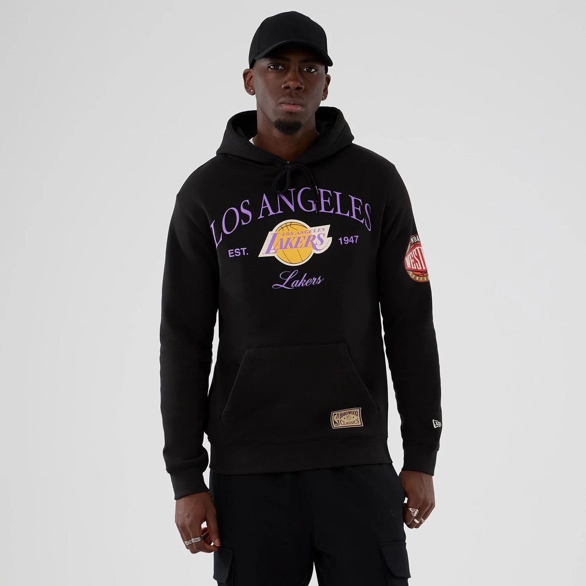 New Era LA Lakers NBA Hardwood Classic Black Pullover Hoodie, front view on-model showing purple Los Angeles Lakers lettering and logo across the chest, a badge on the left sleeve, and a small New Era embroidered logo on the cuff.