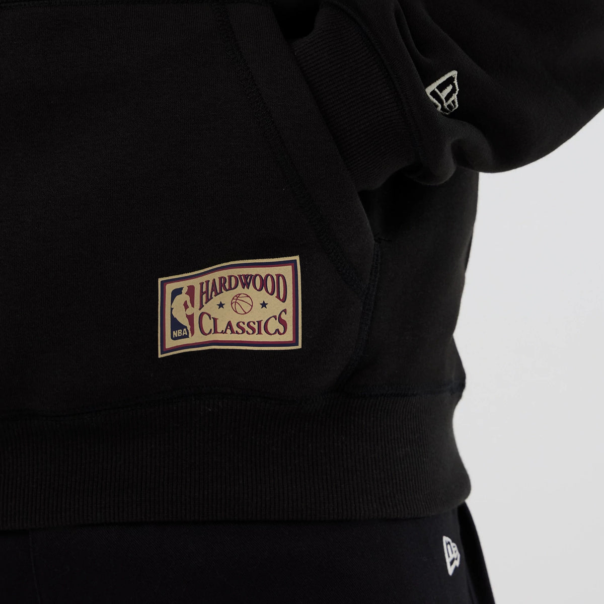 New Era Chicago Bulls NBA Hardwood Classic Black Pullover Hoodie, side view showing a large embroidered Hardwood Classics patch on the lower left side and a small embroidered New Era logo on the sleeve.