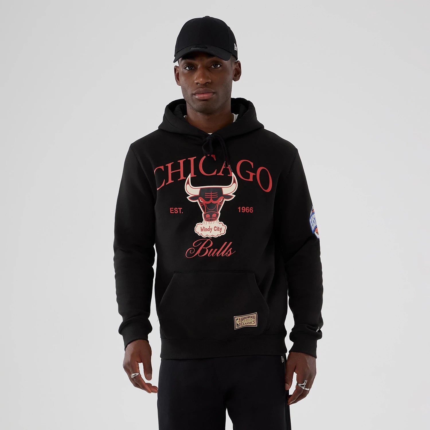 New Era Chicago Bulls NBA Hardwood Classic Black Pullover Hoodie, front view on a model showing the large red and white Bulls logo and lettering on the chest, NBA patch on the sleeve, and Hardwood Classics patch near the hem.