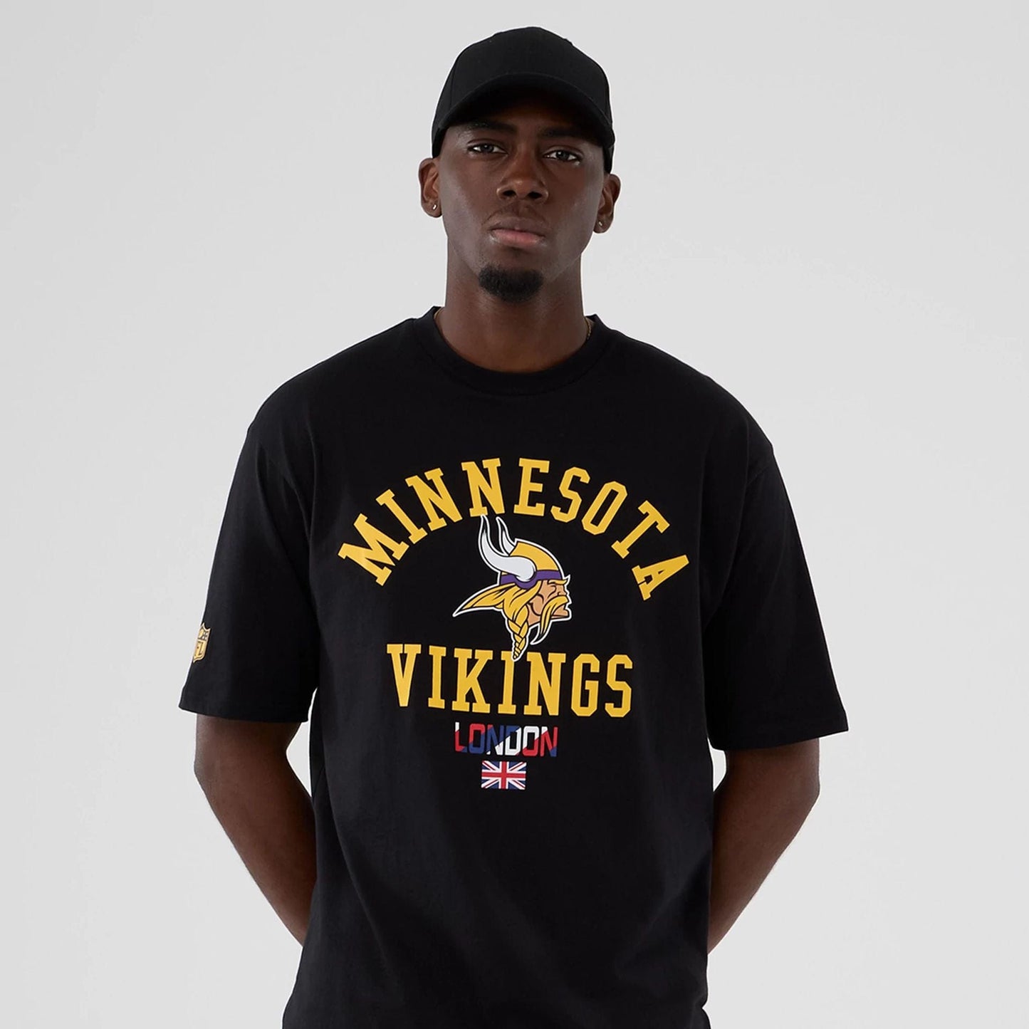 The Male model is wearing Minnesota Vikings NFL International Series Games 2025 Black Oversized T-Shirt 7