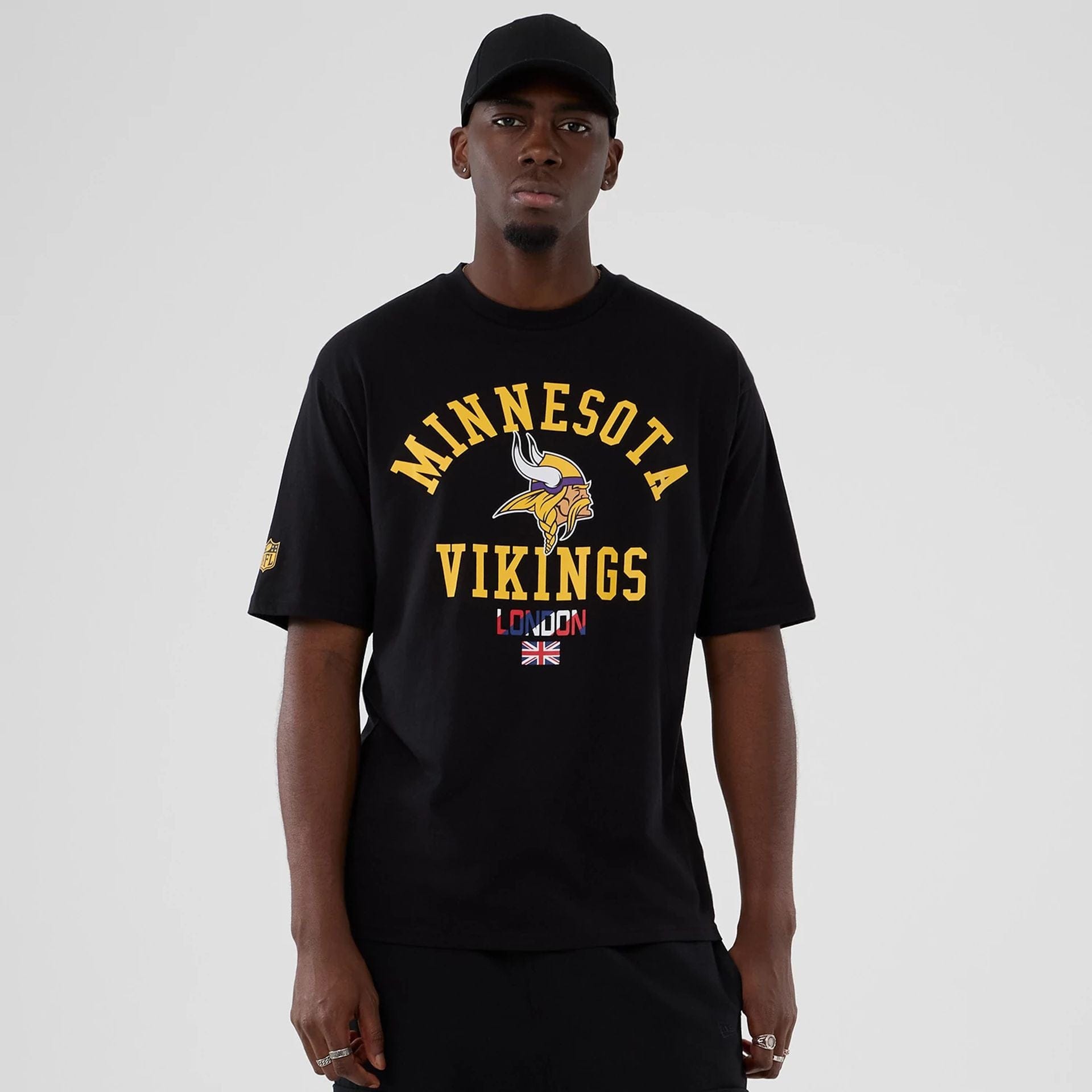 The Male model is wearing Minnesota Vikings NFL International Series Games 2025 Black Oversized T-Shirt 1