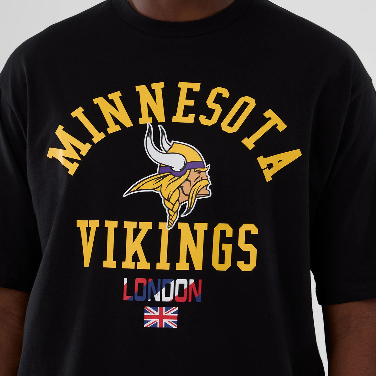 New Era Minnesota Vikings NFL International Series Games 2025 Black Oversized T-Shirt, front view showing a yellow arched Minnesota Vikings graphic with a Viking head beneath, London text in red and navy, and a Union Jack flag printed below.