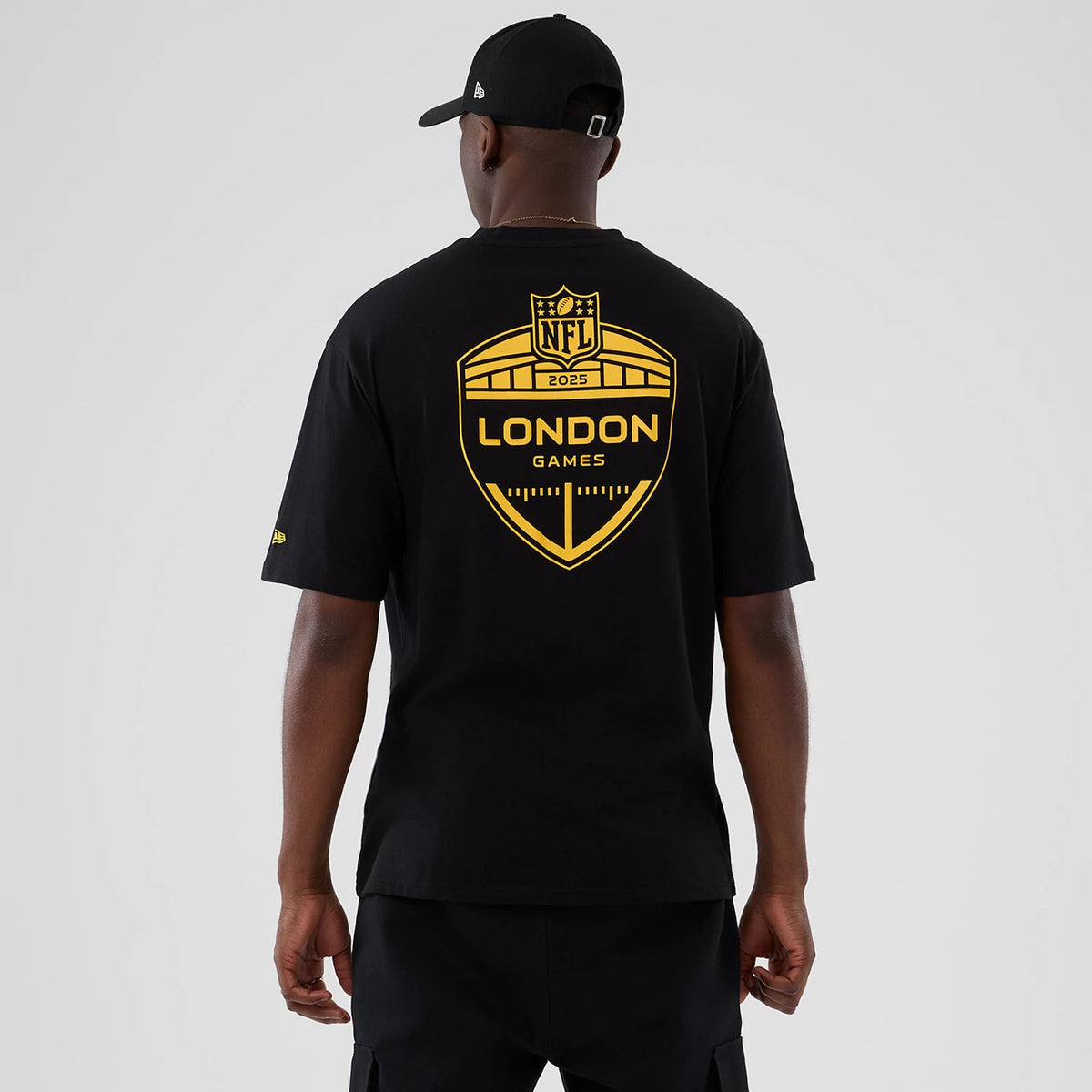 New Era Minnesota Vikings NFL International Series Games 2025 Black Oversized T-Shirt, back view on-model showcasing a large gold printed shield logo reading London Games 2025 across the back, with a small embroidered New Era logo on the sleeve.