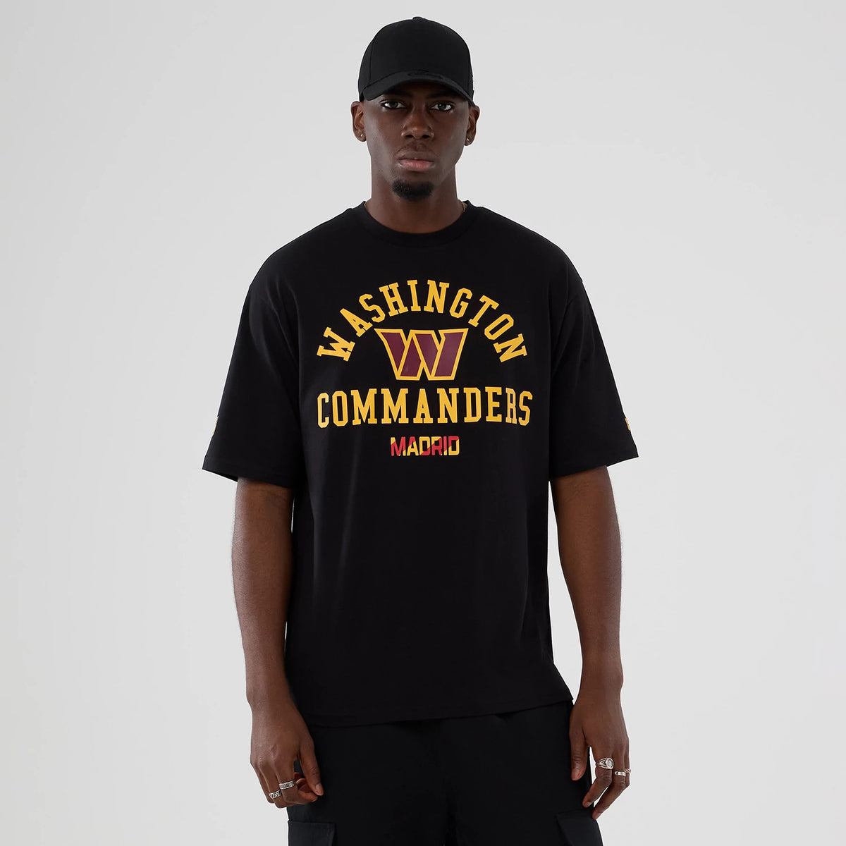 New Era Washington Commanders NFL International Series Games 2025 Black Oversized T-Shirt, front view on a model, featuring yellow Washington Commanders lettering, a large graphic logo in the centre and Madrid text below, all set on a black backdrop.