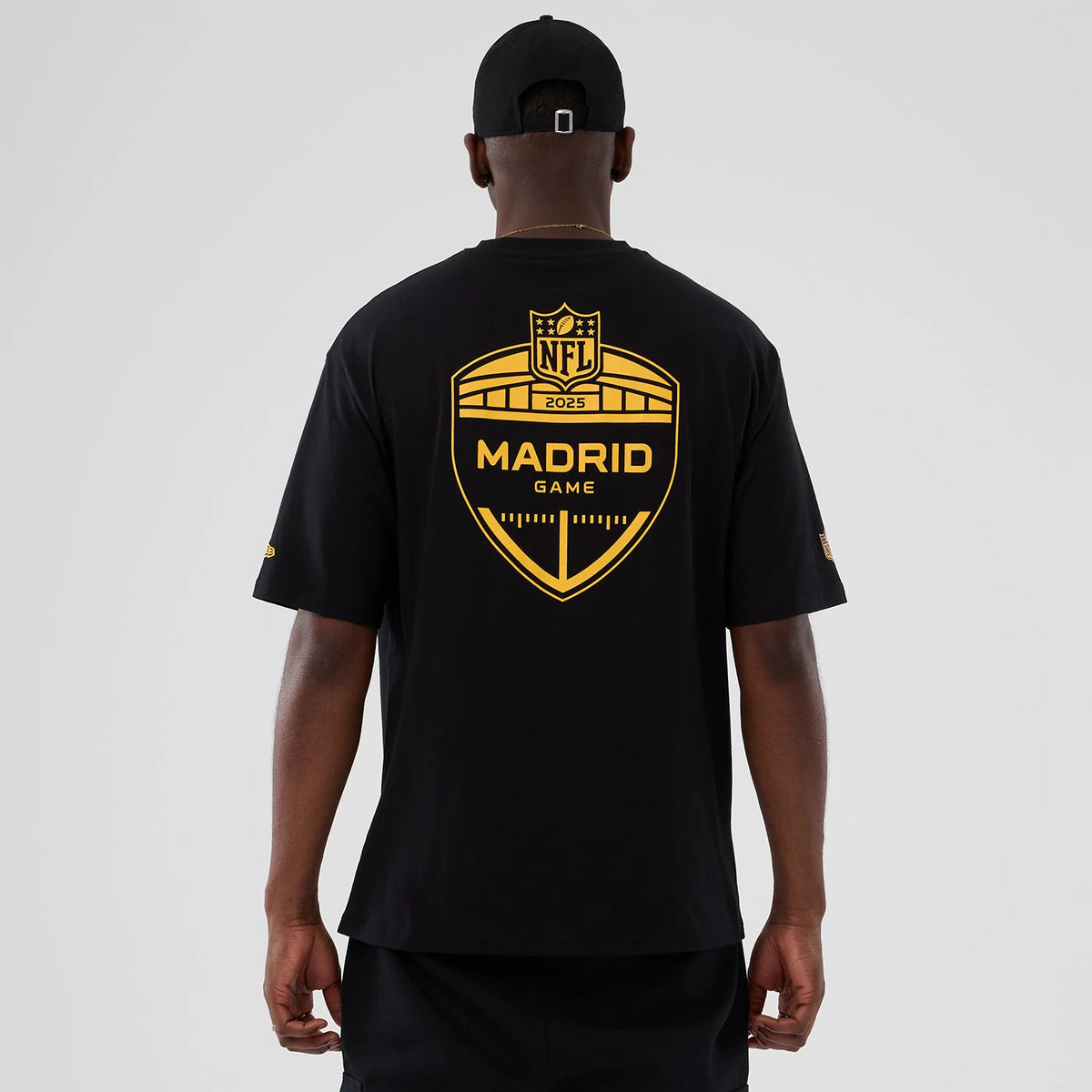 New Era Washington Commanders NFL International Series Games 2025 Black Oversized T-Shirt, back view showing the large yellow printed logo featuring 'NFL 2025 Madrid Game' across the shoulders, worn by a model in black shorts with a black cap.