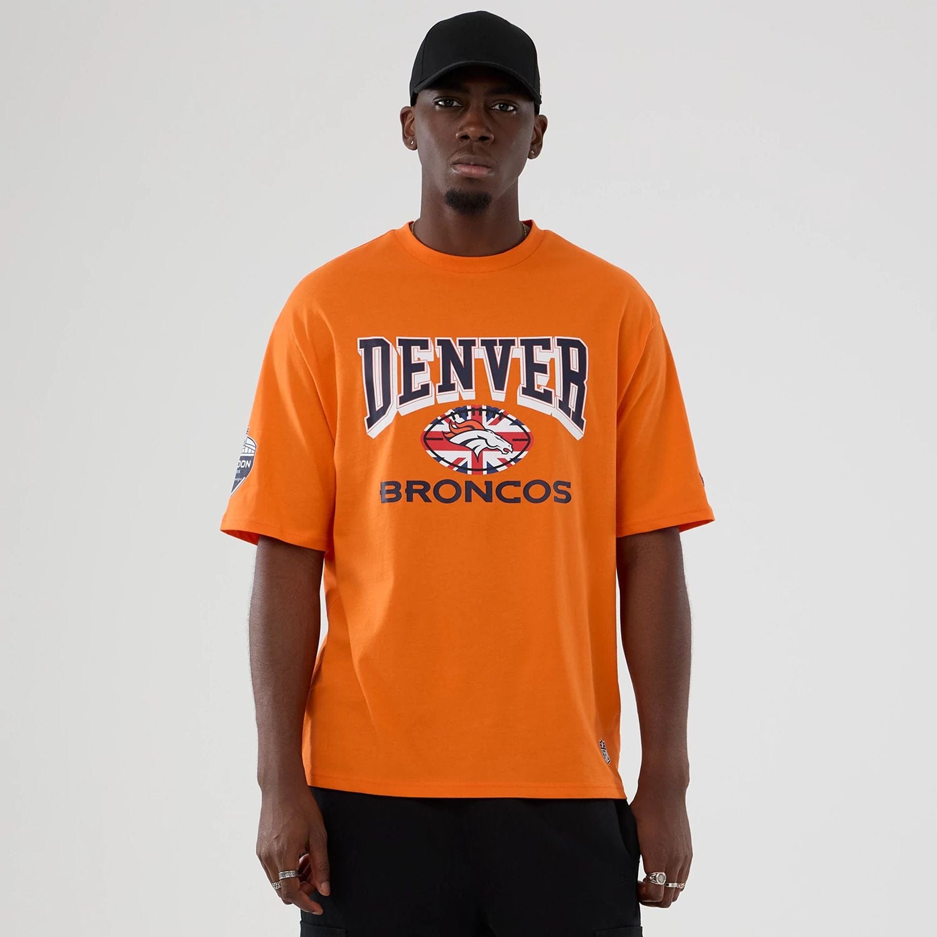 The Male model is wearing Denver Broncos NFL International Series Games 2025 Orange Oversized T-Shirt 1