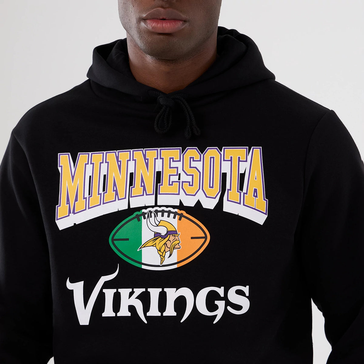 New Era Minnesota Vikings NFL International Series Games 2025 Black Pullover Hoodie, front view showing the printed Minnesota Vikings logo with lettering above and below a football featuring the team emblem on an Irish flag background.