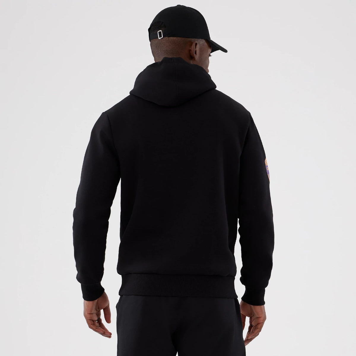 New Era Minnesota Vikings NFL International Series Games 2025 Black Pullover Hoodie, back view on a model showing the all-black design with a raised team logo on the right sleeve and ribbed cuffs and hem for a snug fit.