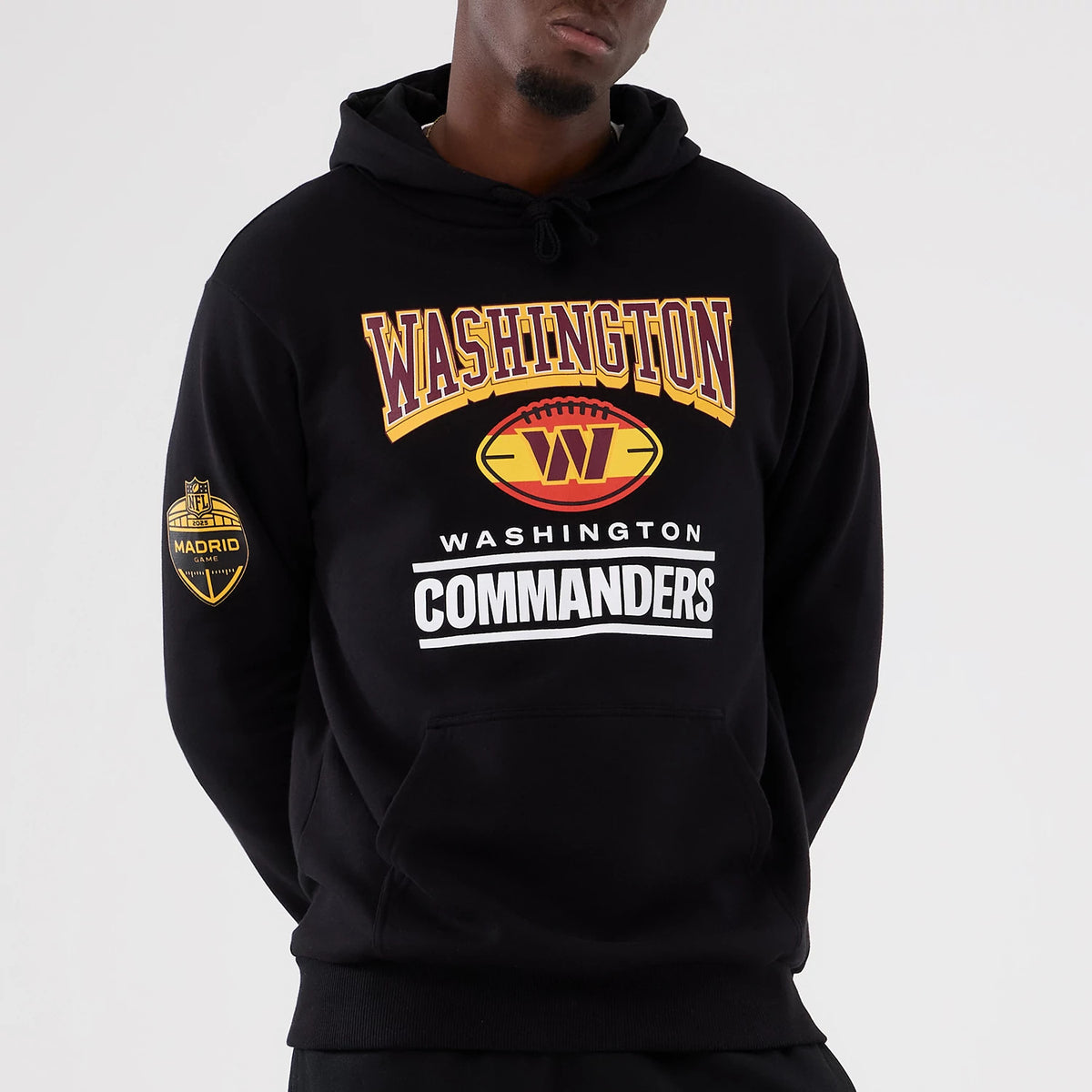 New Era Washington Commanders NFL International Series Games 2025 Black Pullover Hoodie, front view on-model showing large printed Washington and Commanders lettering on the chest and a Madrid Game badge on the left sleeve.