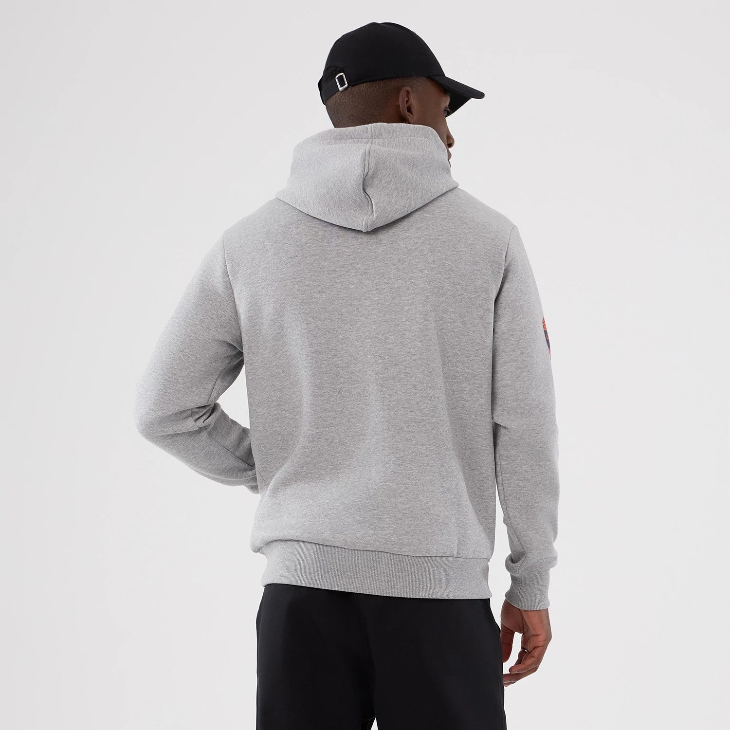 New Era Denver Broncos NFL International Series Games 2025 Grey Pullover Hoodie, back view on a model with a black cap, showcasing the plain grey hooded back and a small embroidered patch on the right sleeve.