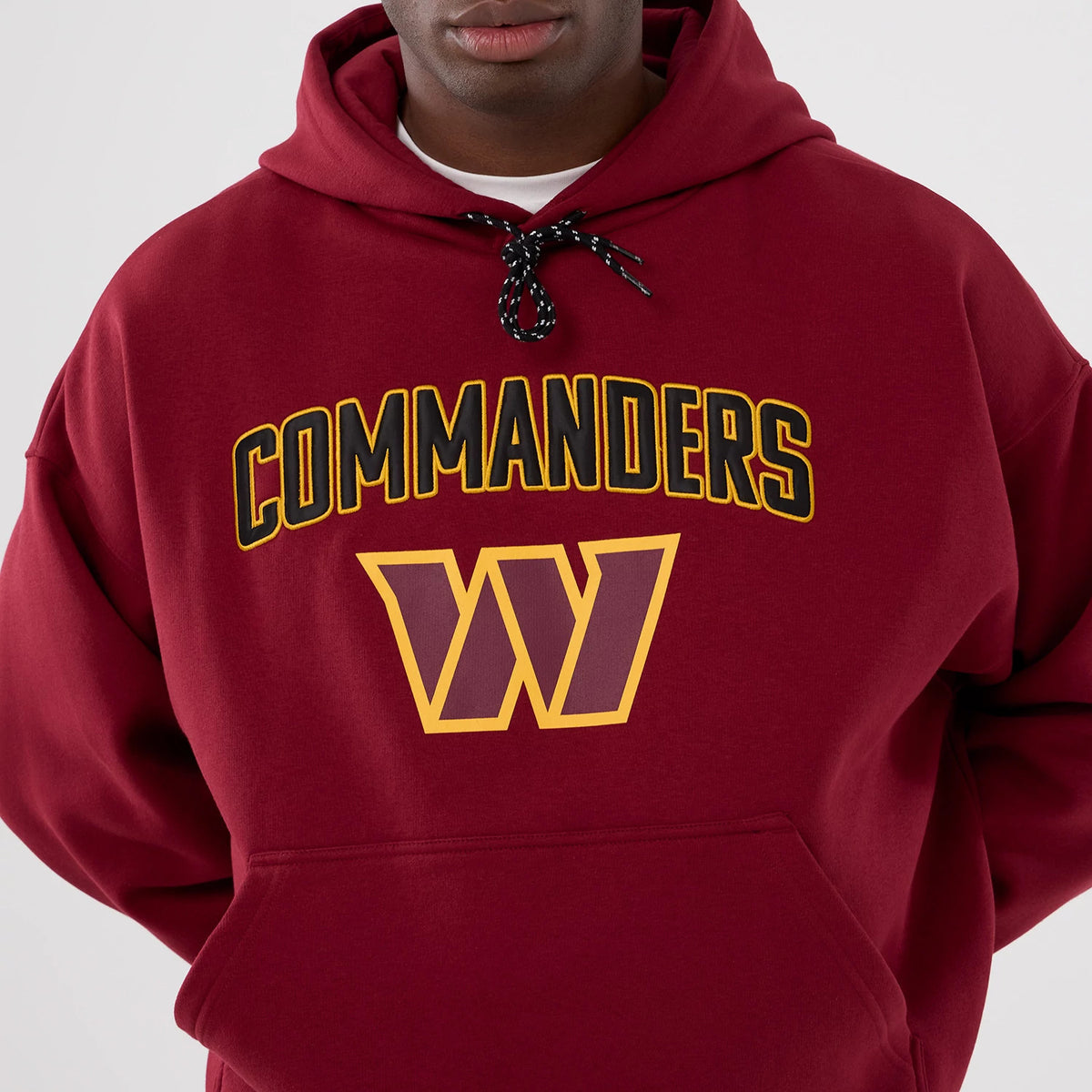 New Era Washington Commanders NFL International Series Games 2025 Dark Red Premium Pullover Hoodie, front view on-model showing an embroidered Commanders logo in gold and black above a large W in yellow on the chest.