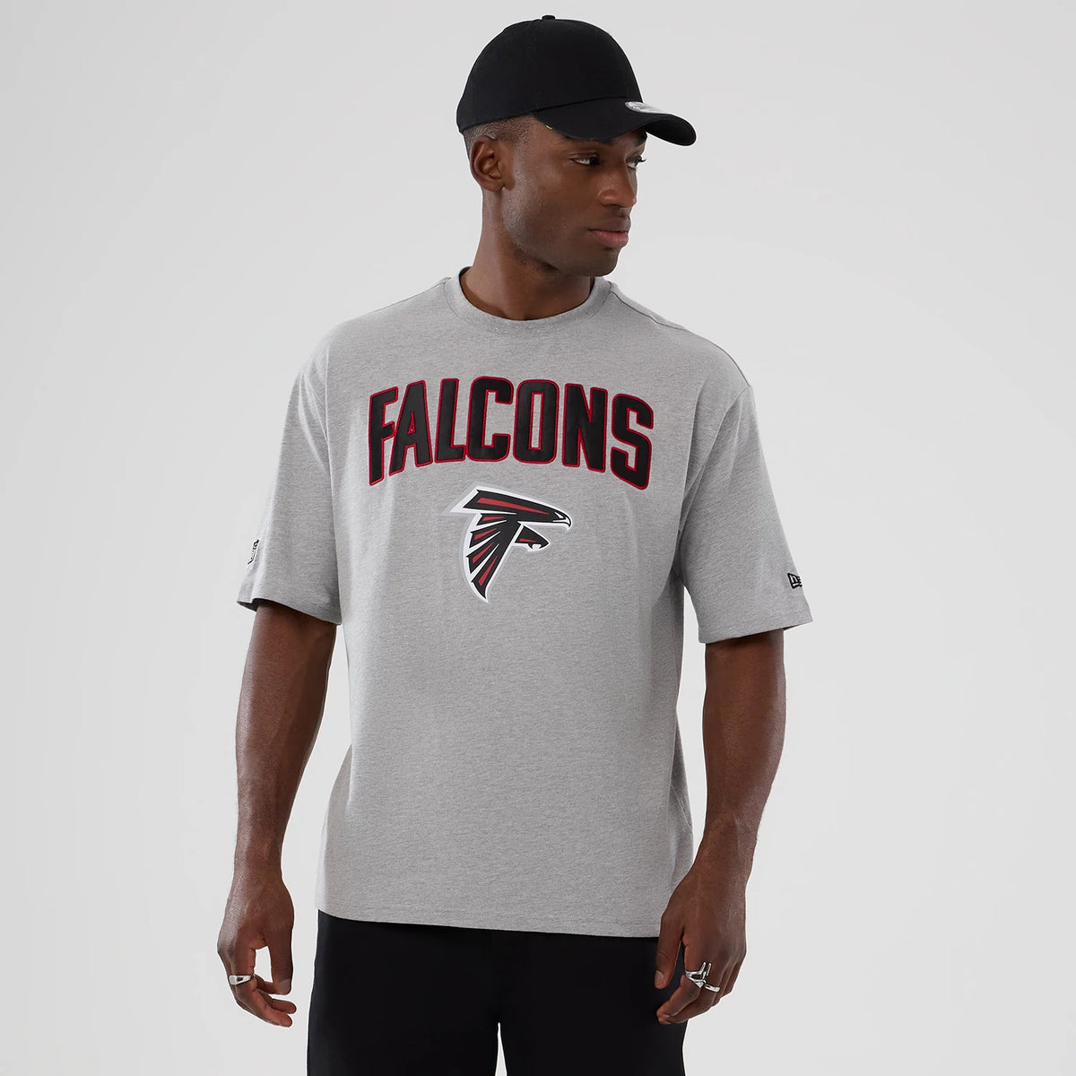 New Era Atlanta Falcons NFL International Series Games 2025 Grey Premium T-Shirt, front view on-model showing black and red Falcons lettering across the chest with the team logo underneath, and a small embroidered New Era logo on the sleeve.