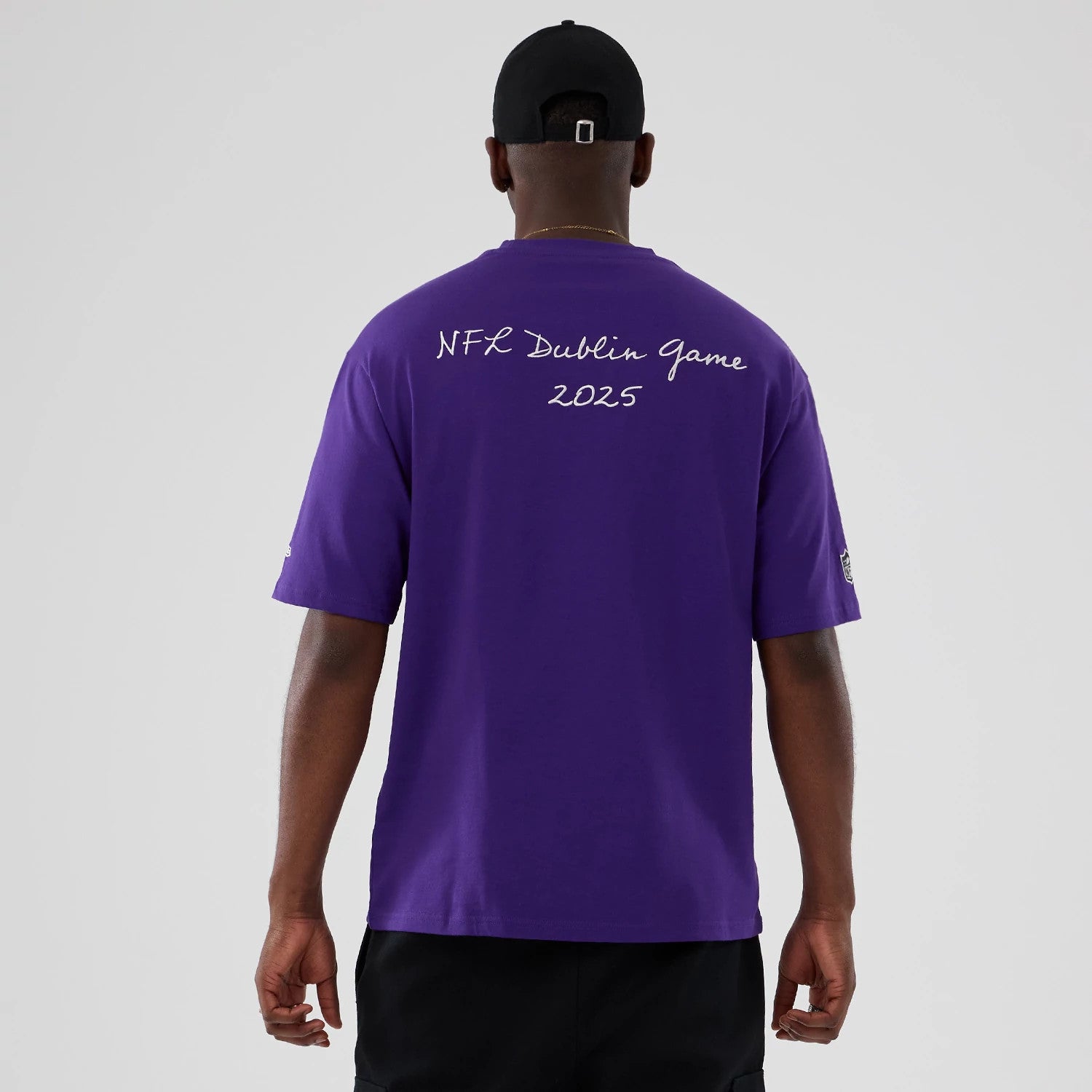 New Era Minnesota Vikings NFL International Series Games 2025 Purple Premium T-Shirt, back view on a model showing the white printed text NFL Dublin Game 2025 across the shoulders and an embroidered New Era logo on the left sleeve.