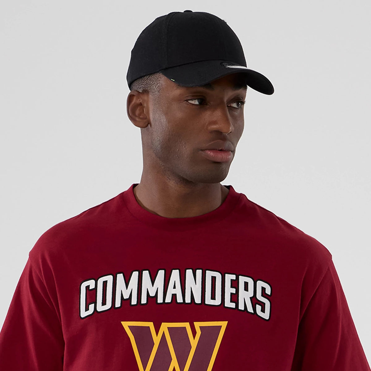 New Era Washington Commanders NFL International Series Games 2025 Dark Red Premium T-Shirt, front view on-model displaying Commanders lettering with a large W below on the chest, styled with a plain black cap.
