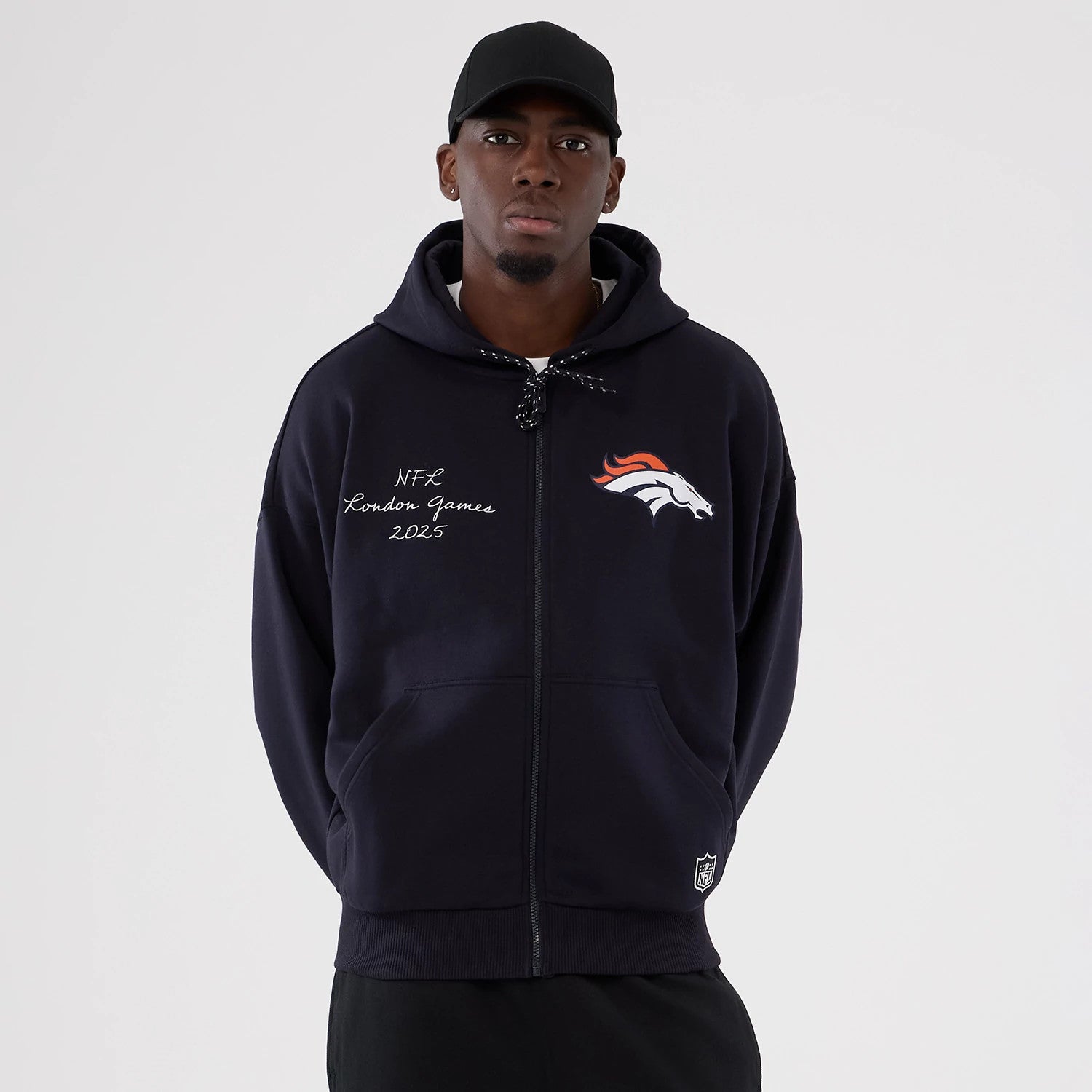 New Era Denver Broncos NFL International Series Games 2025 Navy Premium Pullover Hoodie, front view on-model displaying the Denver Broncos embroidered logo on the chest, with NFL London Games 2025 lettering on the left side above the pocket.