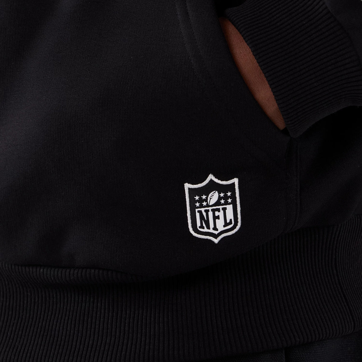 New Era Minnesota Vikings NFL International Series Games 2025 Black Premium Pullover Hoodie, front view showing a white embroidered NFL logo near the lower hem, with ribbed cuffs and a hand tucked into the kangaroo pocket.