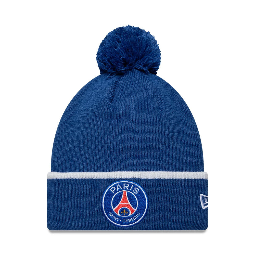 New Era Paris Saint-Germain Core Blue Cuff knit Beanie Hat, front view showing the embroidered PSG club crest centred on the blue fold-over cuff beneath a fluffy blue pom-pom, with the New Era flag logo on the side.