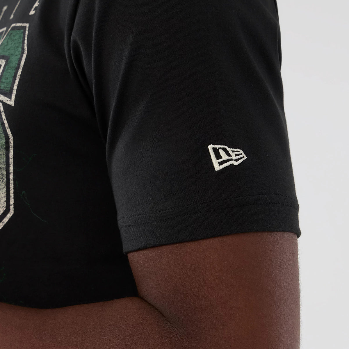 New Era Seattle Supersonics NBA Hardwood Classic Black T-Shirt, side view showing a short sleeve with an embroidered white New Era logo near the hem and part of a large distressed green graphic on the front.