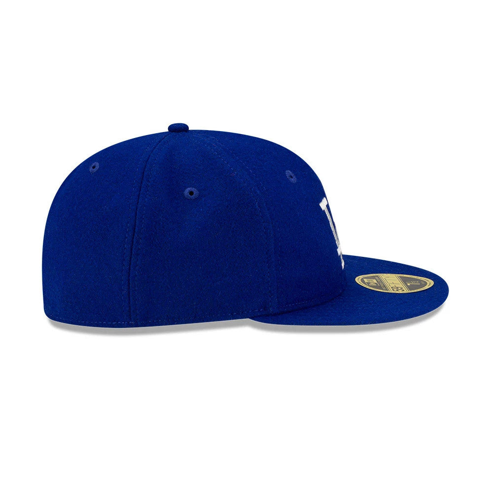 LA Dodgers FOG X MLB Dark Blue Retro Crown New Era 59FIFTY Fitted Cap, side view showing the structured dark blue crown with blue eyelets, the gold 59FIFTY size sticker on the flat visor, and part of the white embroidered logo.