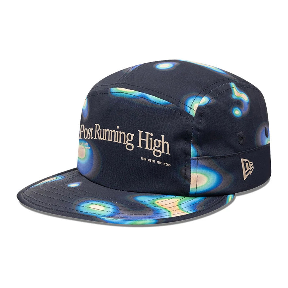 Hermanos Koumori x New Era Navy Camper Cap, three-quarter view showing intricate blue and green heatmap pattern on the navy fabric, with Post Running High text on the front panel and the New Era flag logo on the left side.