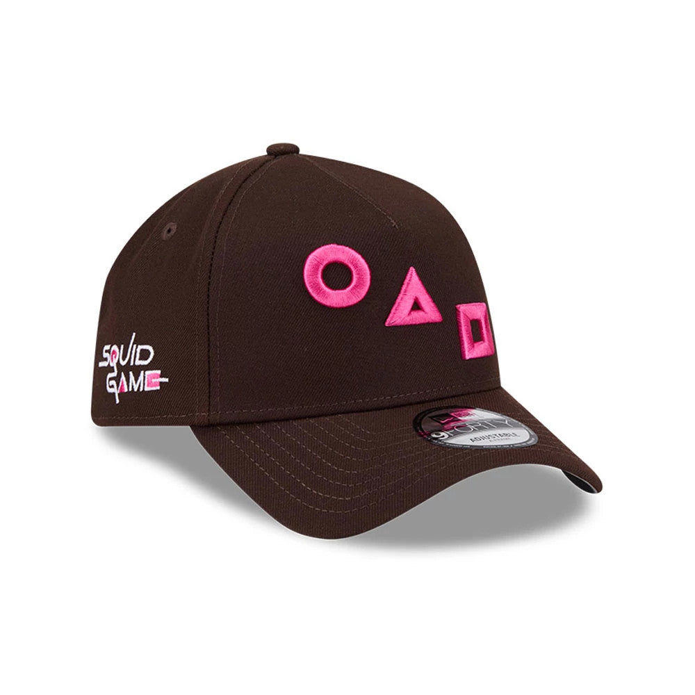 Netflix Squid Game Shapes Dark Brown New Era 9FORTY A-Frame Adjustable Cap, three-quarter view showing pink embroidered circle, triangle, and square shapes on the front panel, with a Squid Game logo on the left side.