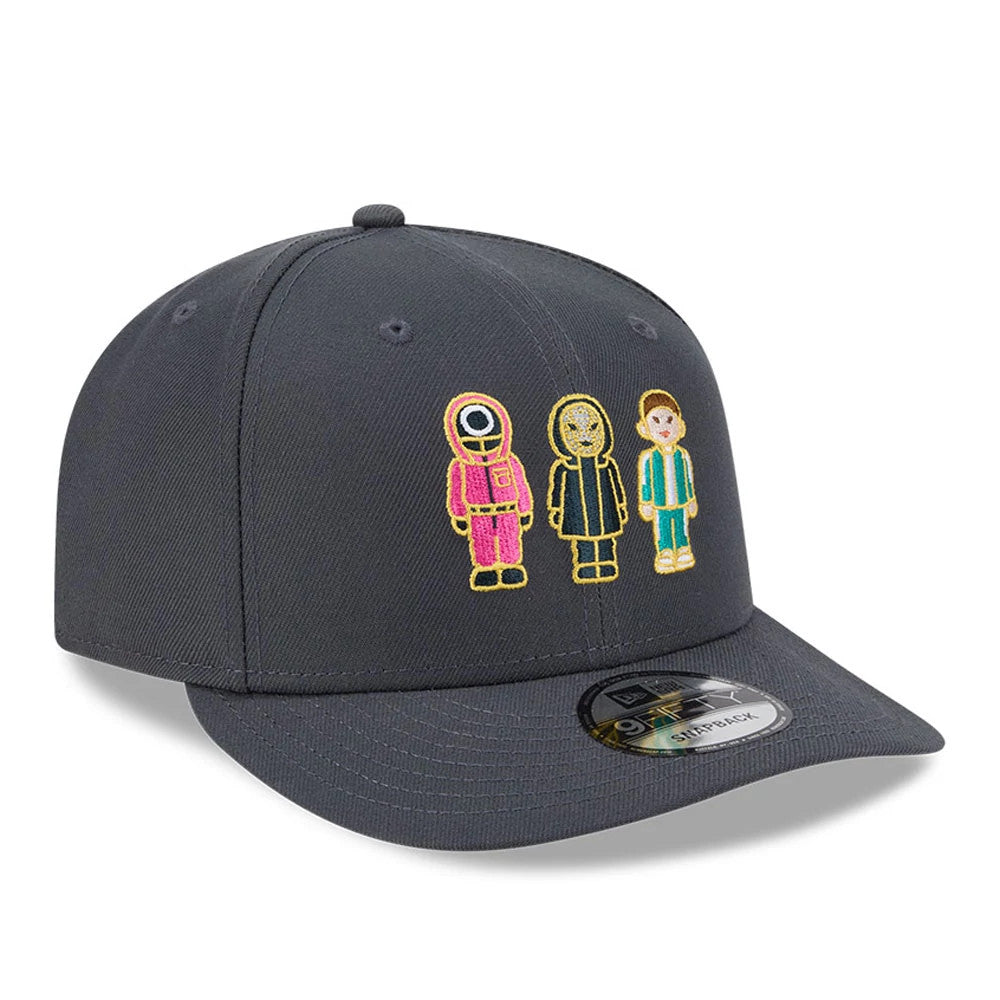 Netflix Squid Game Dark Grey New Era 9FIFTY Snapback Adjustable Cap, three-quarter view showing colourful embroidered characters from the series on the front panel, grey structured crown and a black 9FIFTY size sticker on the dark grey flat visor.
