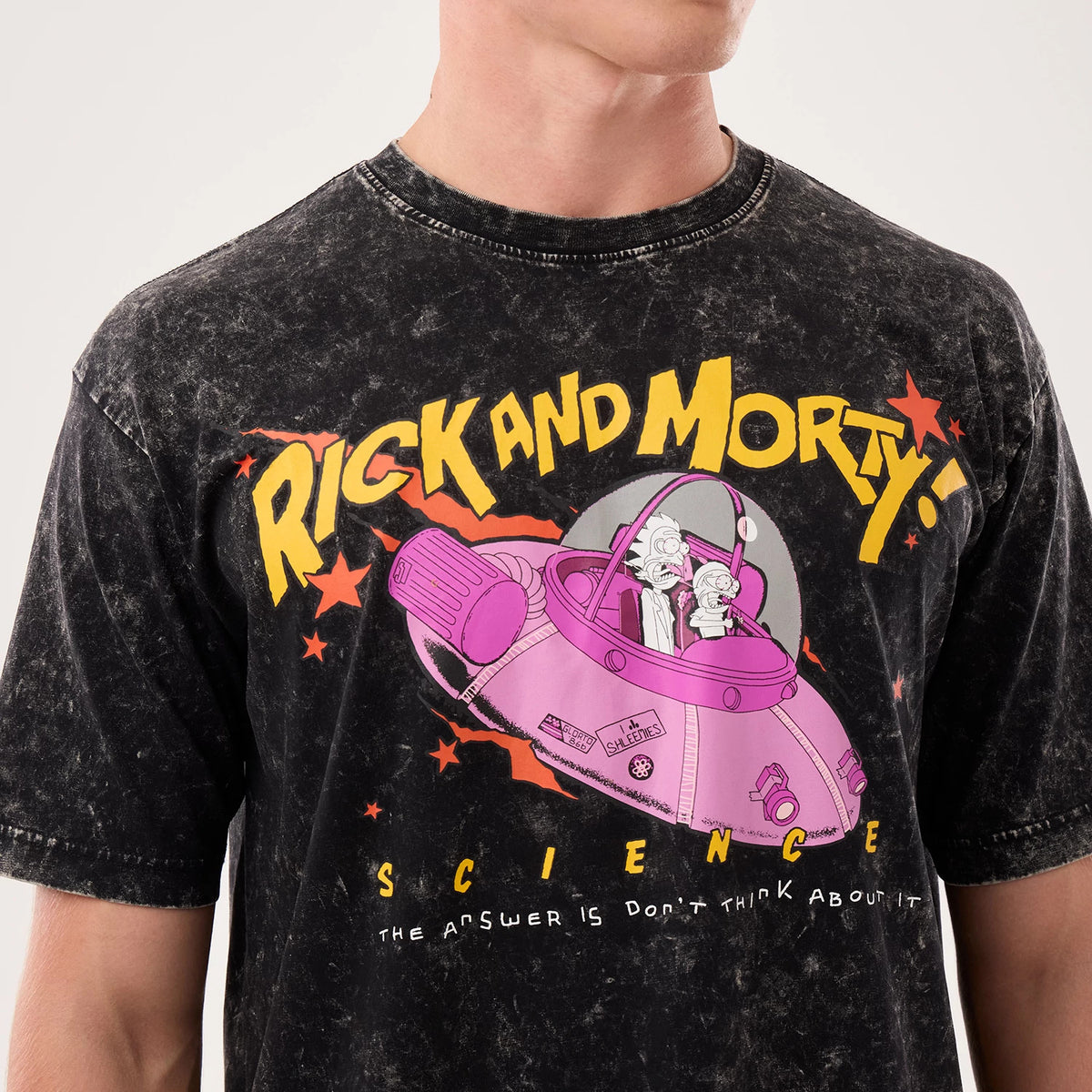 New Era Rick And Morty Science Black T-Shirt, front view showing a graphic of a pink spaceship with characters inside, large yellow Rick and Morty lettering across the upper front, and small stars around the design on a marbled black background.