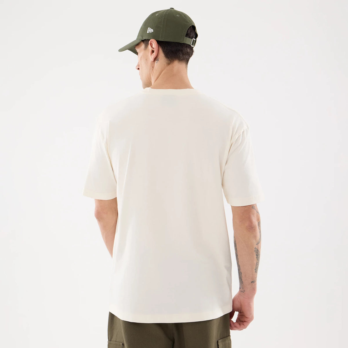 New Era LA Dodgers MLB Life Graphic Light Beige T-Shirt, back view on-model showing plain light beige fabric with a relaxed fit and short sleeves, paired with dark green trousers and a matching cap with an embroidered New Era logo on the side.