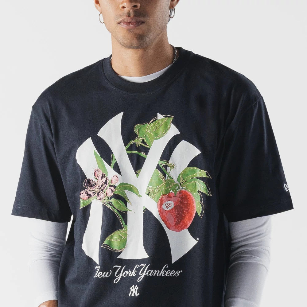 New Era New York Yankees MLB Life Graphic Navy T-Shirt, front view on-model featuring a large white New York Yankees logo adorned with floral graphics and a red apple, with an embroidered New Era logo on the sleeve and layered over a white top.