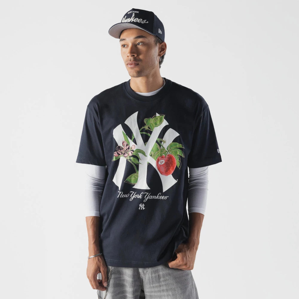 New Era New York Yankees MLB Life Graphic Navy T-Shirt, front view on-model showing a large printed New York Yankees logo adorned with floral graphics and a red apple, with New York Yankees text beneath.