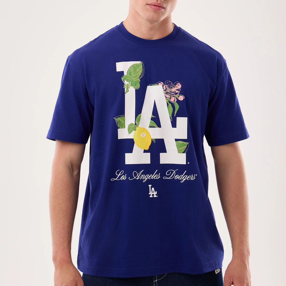 New Era LA Dodgers MLB Life Graphic Dark Blue T-Shirt, front view on a model featuring a large white LA logo with floral and lemon graphics, elegant cursive Los Angeles Dodgers text below, and a small white LA logo near the hem.
