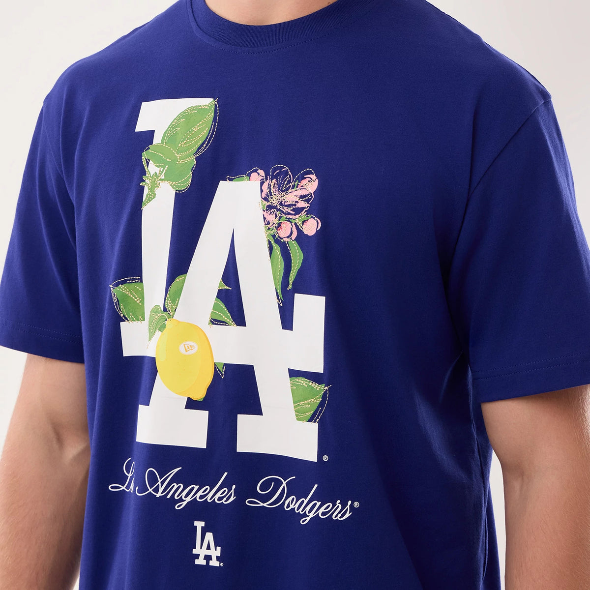 New Era LA Dodgers MLB Life Graphic Dark Blue T-Shirt, front view showing a large white printed LA logo with floral and lemon designs, the script 'Los Angeles Dodgers' lettering below, and a small white LA logo near the hem, worn by a model.