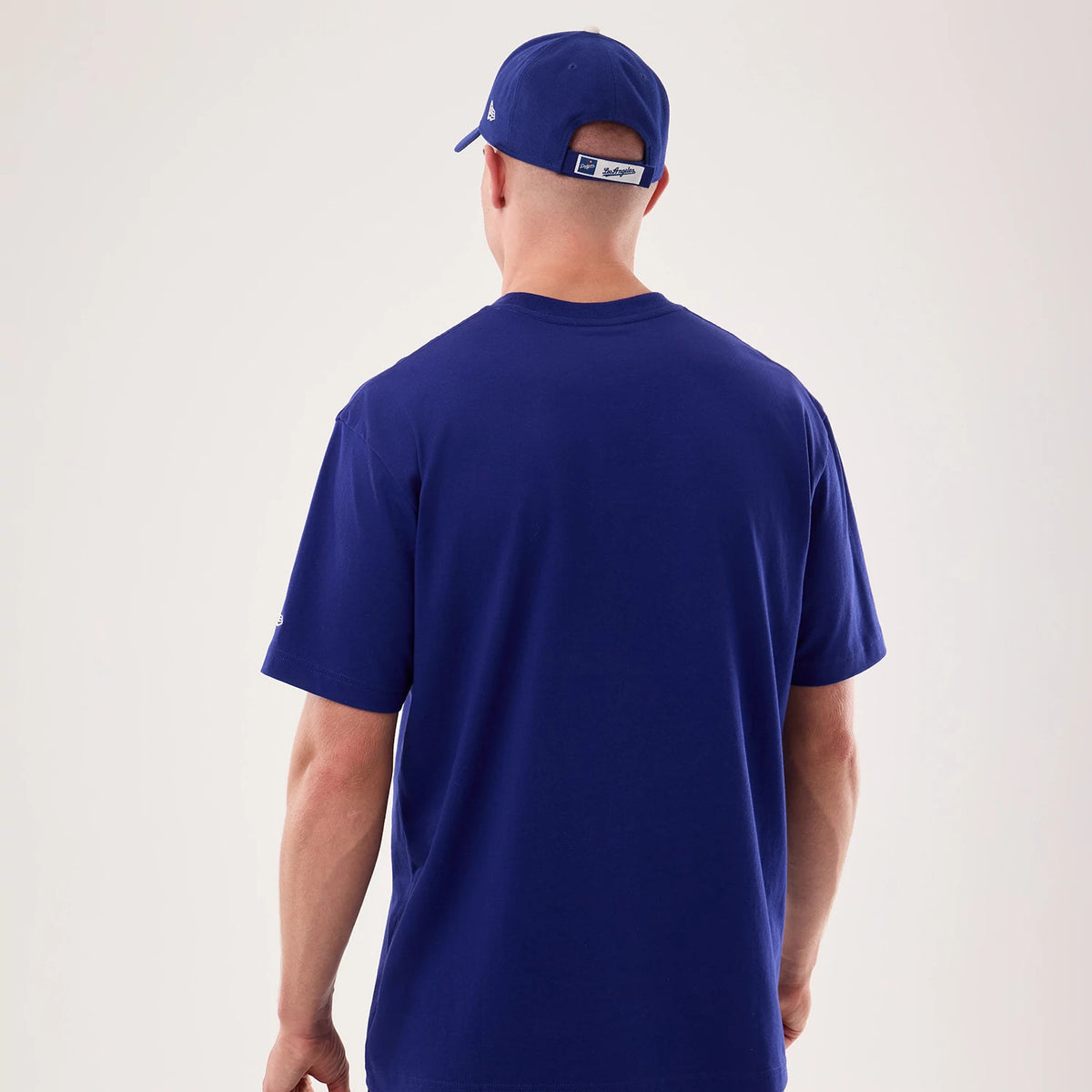 New Era LA Dodgers MLB Life Graphic Dark Blue T-Shirt, back view on a model paired with a matching cap, showing a plain dark blue back with short sleeves, and an embroidered New Era logo on the left sleeve and side of the cap.