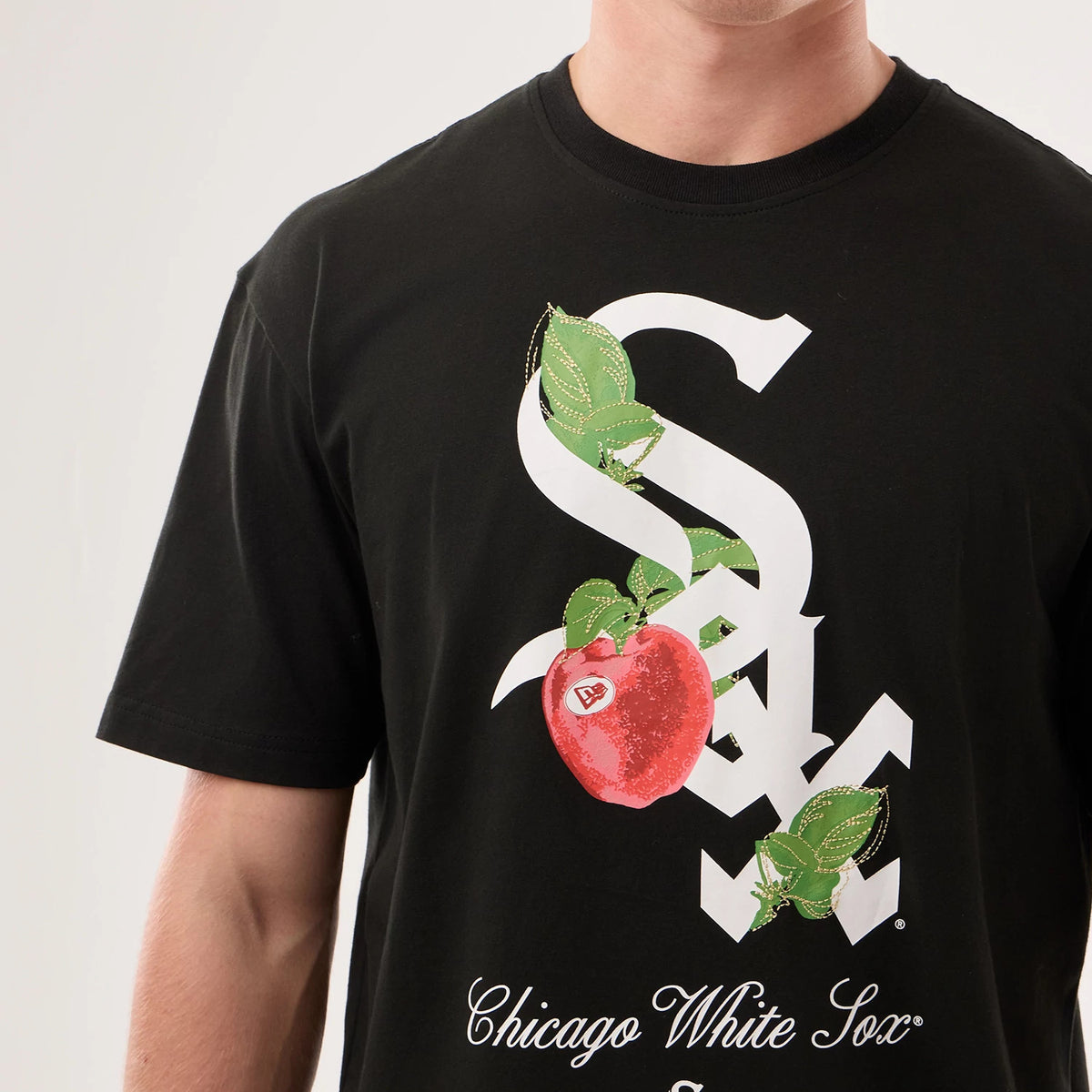 New Era Chicago White Sox MLB Life Graphic Black T-Shirt, front view on a model showing a large white printed logo intertwined with green leaves and a red apple graphic, and elegant white 'Chicago White Sox' lettering across the lower front.