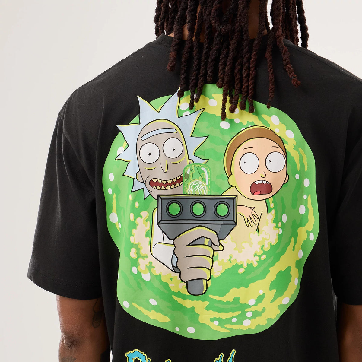 New Era Rick And Morty Portal Gun Black T-Shirt, back view on a model showing a graphic of Rick and Morty emerging from a green portal with a portal gun in the foreground, featuring colours on a plain black background.
