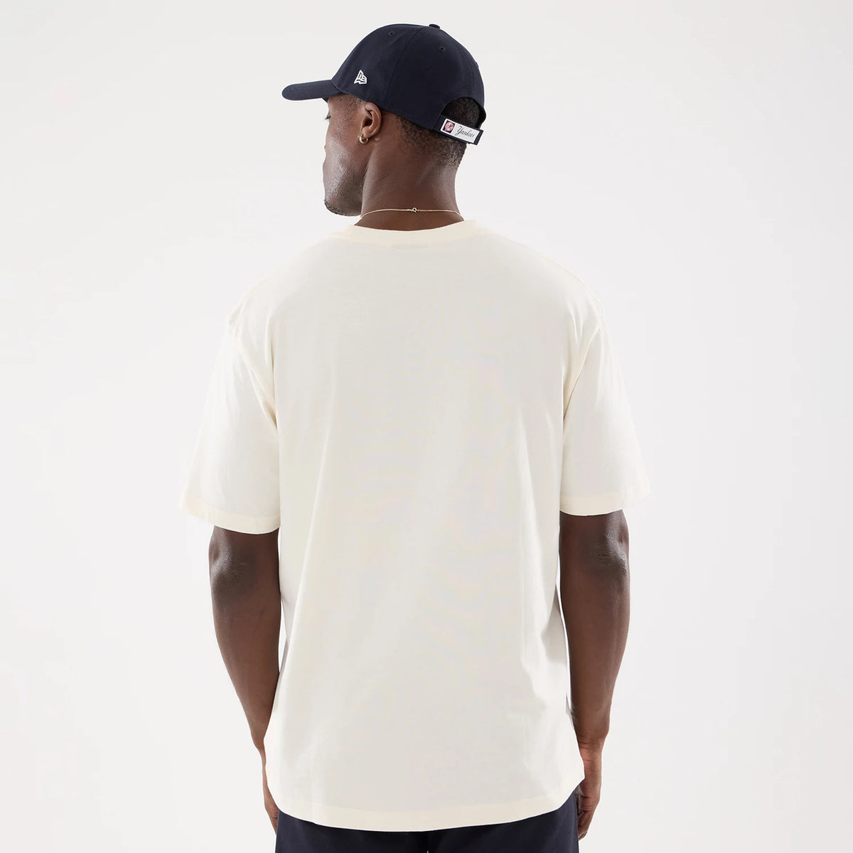 New Era New York Yankees MLB Life Graphic Light Beige T-Shirt, back view on a model styled with a navy cap, showing the plain light beige fabric and short sleeves with no graphics or logos, offering a clean and simple look.