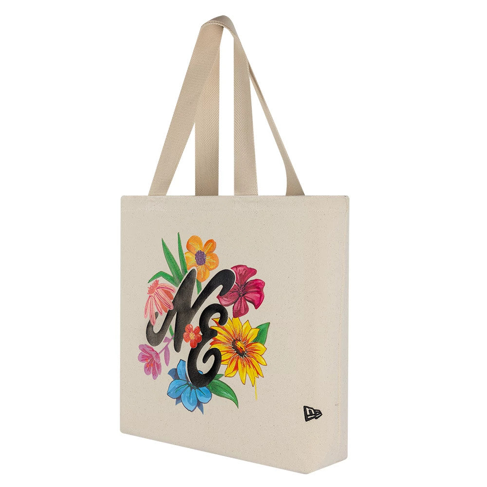 New Era Graphic Light Beige Tote Bag, side view showcasing NE lettering surrounded by colourful flowers on the front, beige handles for carrying positioned at the top and a small embroidered New Era logo at the bottom corner.
